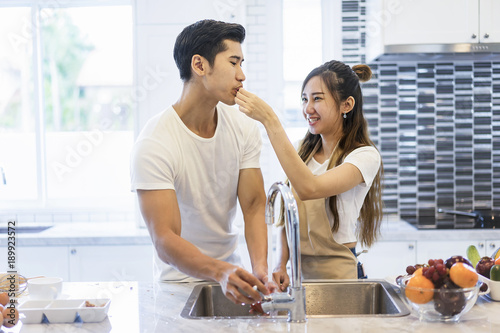 Beautiful asian young couple loving smiling is looking to cooking in kitchen at home.