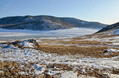 wooded hills and ice covered Tugnuy river on a sunny day in early spring Sagan-Nur, Republic of Buryatia, Russia