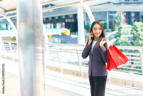 Beautiful shopper woman hand shopping with a smartphone and carrying red bag. concept of woker shopping and business online.