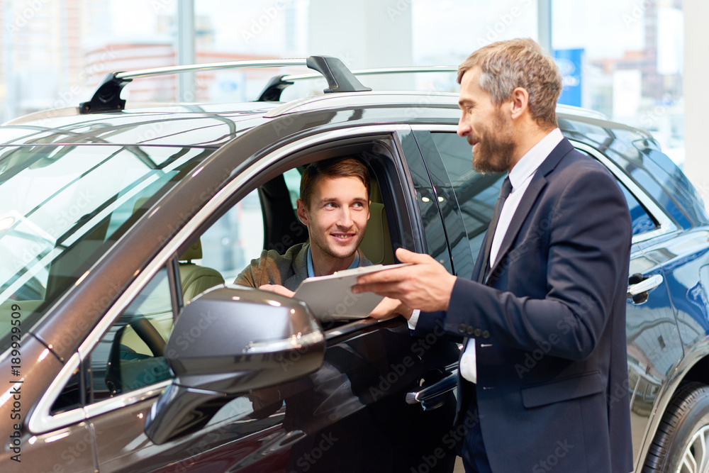Portrait of handsome young man taking luxury car for test drive, sitting inside and smiling at sales manager Portrait of handsome young man taking luxury car for test drive, sitting inside and smiling at sales manager