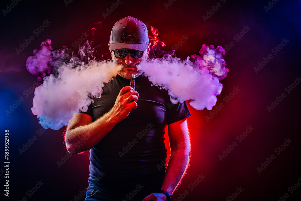 vaping man holding a mod. A cloud of vapor. Black background. vaping man holding a mod. A cloud of vapor.
