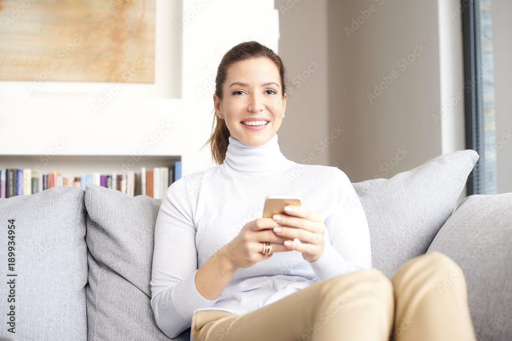 Enjoy my comfy home and chating online. A smiling brunette mature woman relaxing on couch and text messaging on her cell phone. Enjoy my comfy home and chating online. A smiling brunette mature woman relaxing on couch and text messaging on her cell phone.