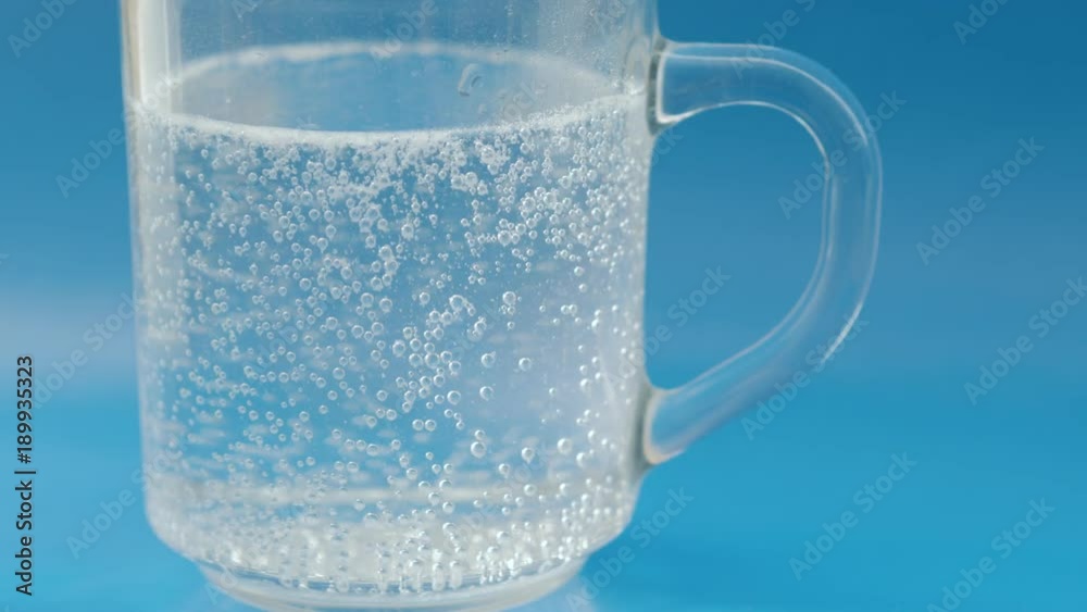 Effervescent pill in a glass of water on blue background. Effervescent pill in a glass of water on blue background.