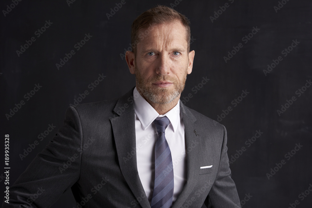 Confident middle aged businessman. Portrait shot of a middle aged businessman wearing suit and looking thoughfully while standing at dark background. Copy space. Confident middle aged businessman. Portrait shot of a middle aged businessman wearing suit and looking thoughfully while standing at dark background. Copy space.