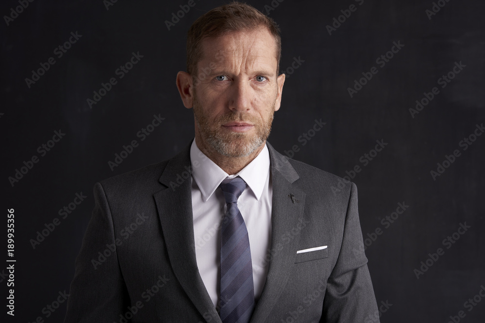 Confident middle aged businessman. Portrait shot of a middle aged businessman wearing suit and looking thoughfully while standing at dark background. Copy space. Confident middle aged businessman. Portrait shot of a middle aged businessman wearing suit and looking thoughfully while standing at dark background. Copy space.