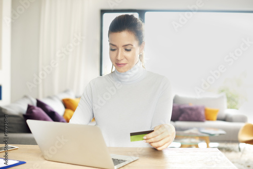 Shopping from home. Attractive woman using her laptop to make online purchases with her credit card while sitting at desk at home. 