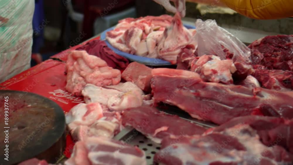The seller cuts and displays meat on a counter. The meat market in Vietnam. Insanitary conditions. Large number of pieces of crude meat. The seller cuts and displays meat on a counter. The meat market in Vietnam. Insanitary conditions. Large number of pieces of crude meat.