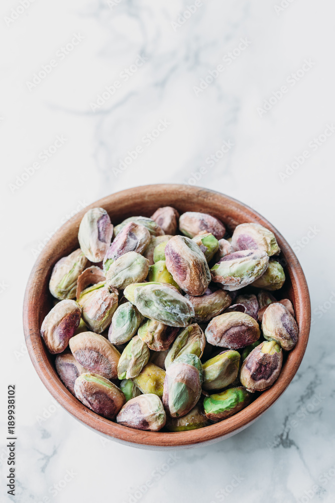 Pistachios in wooden bowl on marble background with copy space Pistachios in wooden bowl on marble background with copy space