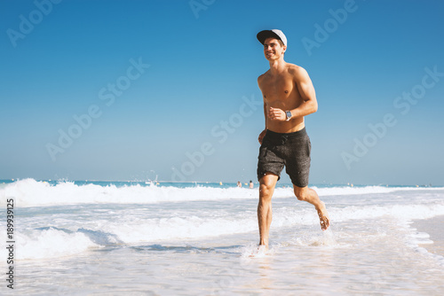  Shirtless young man enjoying jogging outside on the beach.