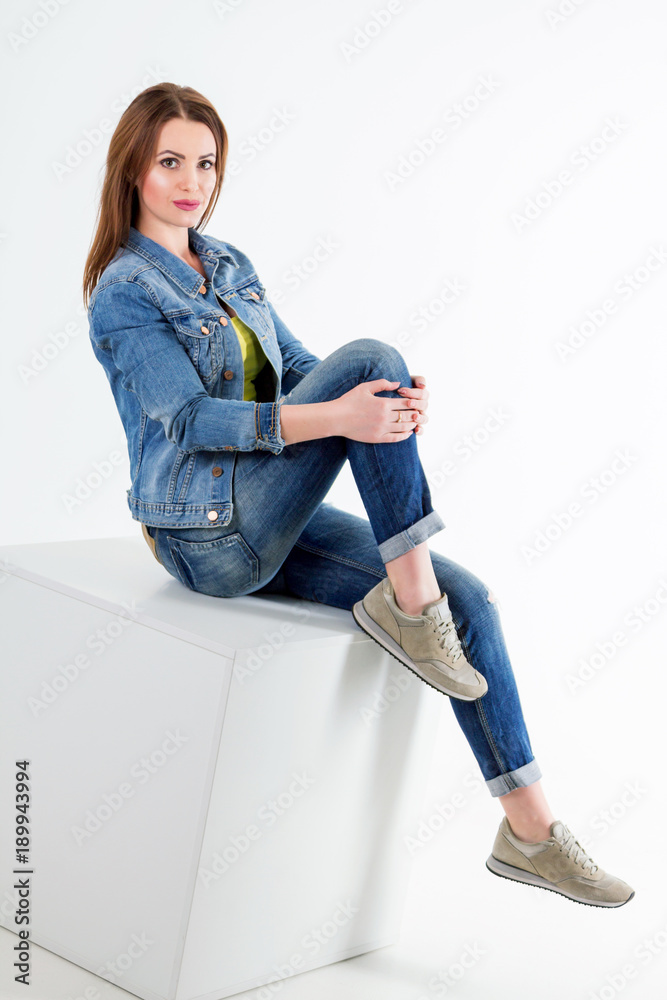 Studio portrait of beautiful young smiling woman wearing blue jeans and  denim jacket, sitting over white background. Casual style. foto de Stock |  Adobe Stock