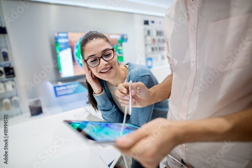 Close up portrait view of cute excited charming young student girl in love looking at a tablet while her boyfriend testing with a pencil in a tech store.