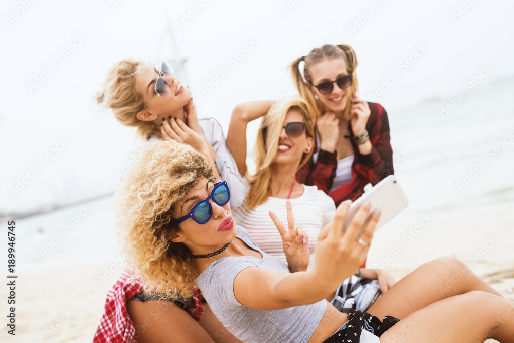 Beautiful joyful girls taking a group selfie with the phone on the beach while having a good time. Beautiful joyful girls taking a group selfie with the phone on the beach while having a good time.