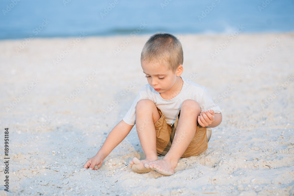 Portrait serious little boy playing in the sand near the sea, ocean. Positive human emotions, feelings, joy. Funny cute child taking vacations and enjoying summer. Portrait serious little boy playing in the sand near the sea, ocean. Positive human emotions, feelings, joy. Funny cute child taking vacations and enjoying summer.