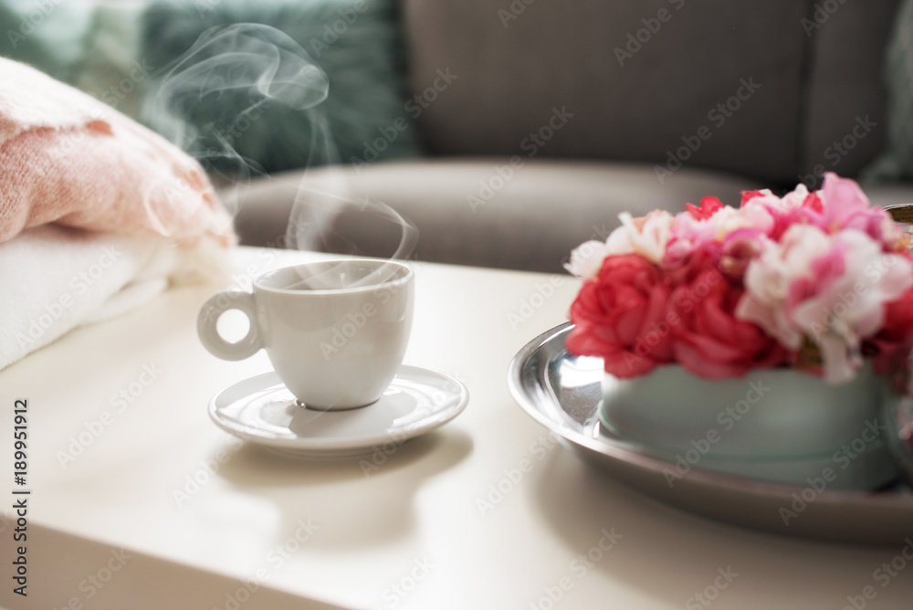 Still life details in home interior of living room. Sweaters and cup of coffe with steam on a serving tray on a coffee table. Breakfast over sofa in morning sunlight. Still life details in home interior of living room. Sweaters and cup of coffe with steam on a serving tray on a coffee table. Breakfast over sofa in morning sunlight.