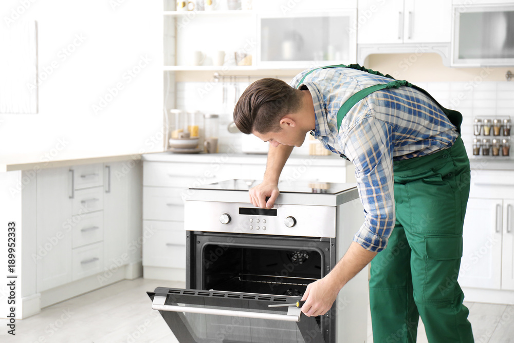 Young man repairing oven in kitchen Young man repairing oven in kitchen