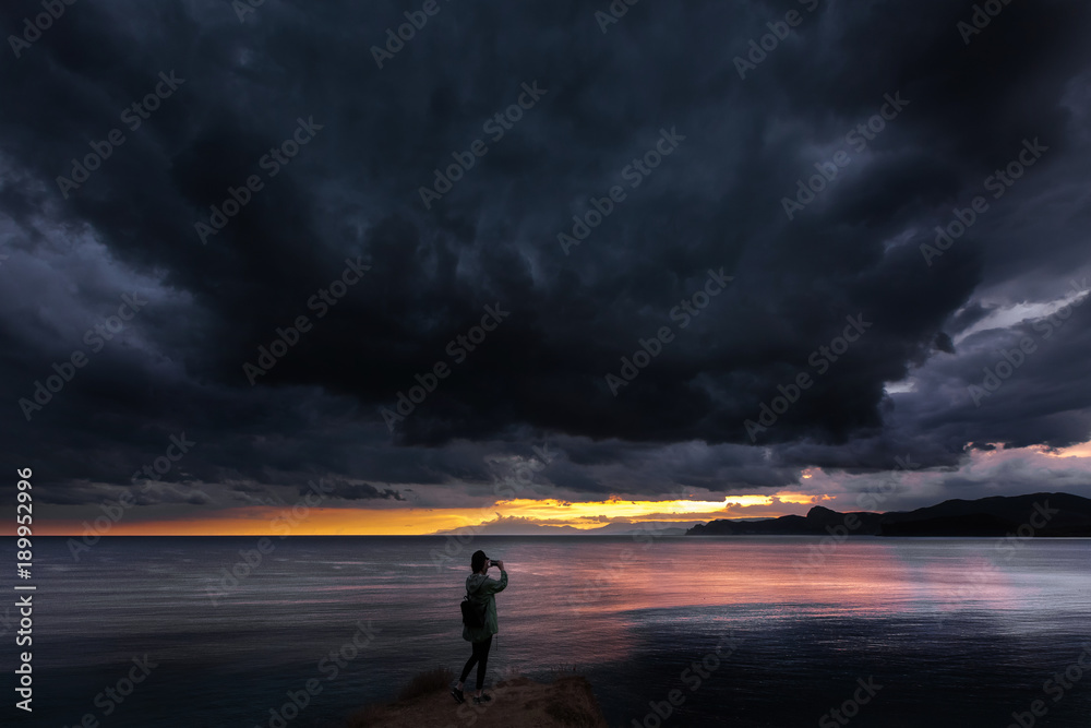girl at the sea in the evening takes pictures of the sunset before the storm