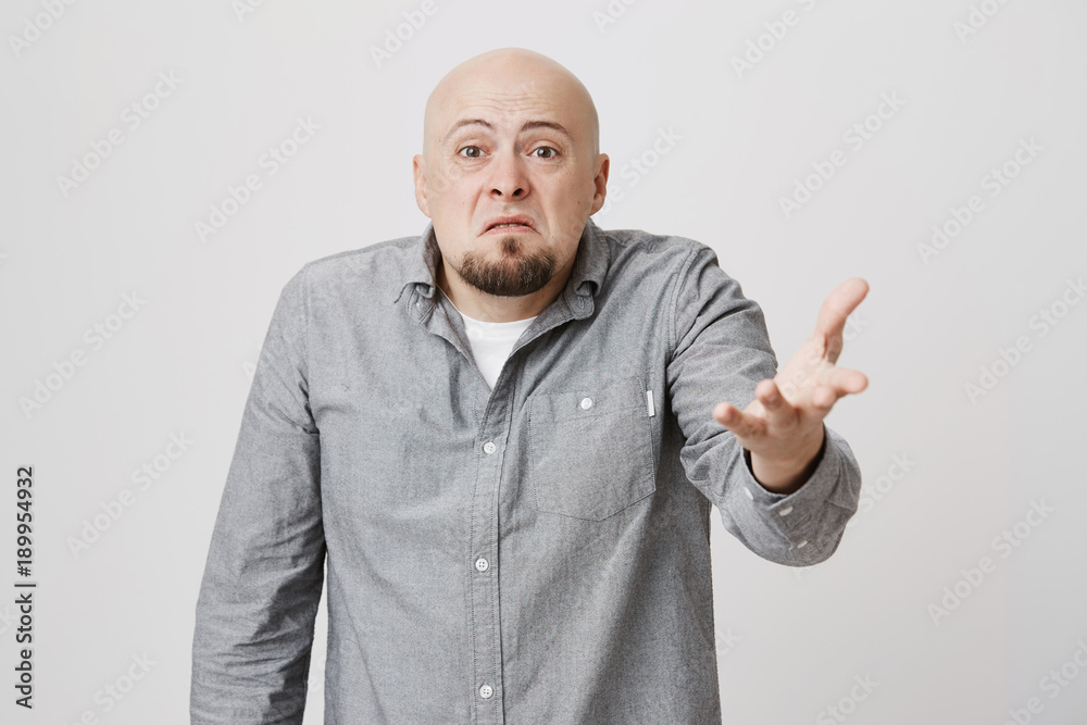 So what, Who cares. Aggressive bald european bearded man wearing gray shirt shrugging his shoulders in questioning gesture of uncertainty and having irritated clueless look So what, Who cares. Aggressive bald european bearded man wearing gray shirt shrugging his shoulders in questioning gesture of uncertainty and having irritated clueless look