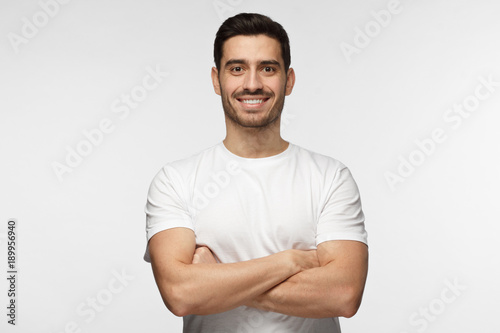 Portrait of smiling handsome man in white tshirt standing with crossed arms isolated on grey background