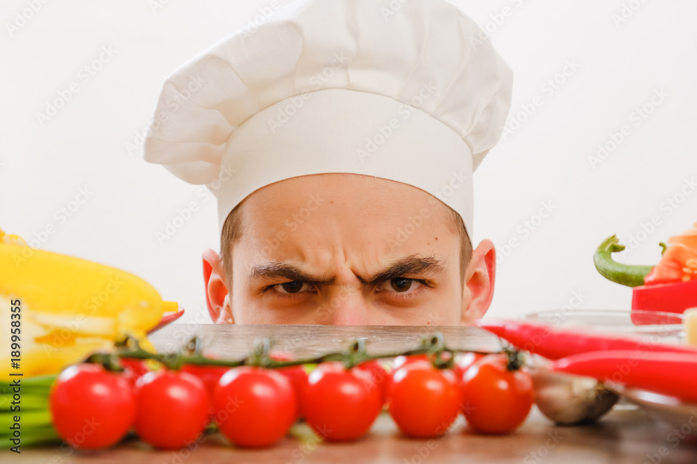 Man with cook cap on white background. Chef with vegetables on table. Cook with cheerful face in face close up.