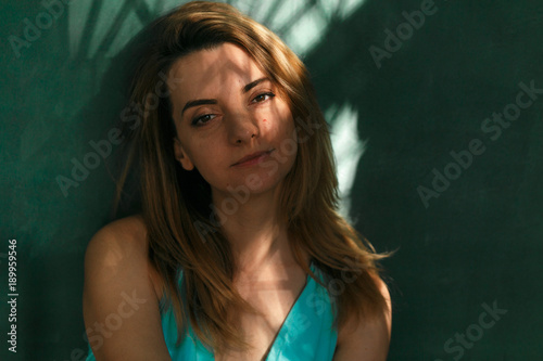 Tender woman sits on floor barefoot against green wall. Relaxing in sunbeams