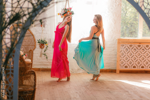 Two attractive women dancing in colored dresses bare foot on wooden floor in old fashioned room