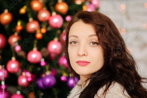 Beautiful Female Face with Perfect Skin and Sensual Lips on the Background of a Christmas Tree with Colorful Glass Balls.