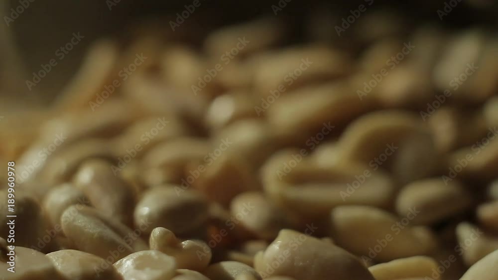 Peeled peanuts are fried in a pan. Hand with a spoon stirring nuts Peeled peanuts are fried in a pan. Hand with a spoon stirring nuts