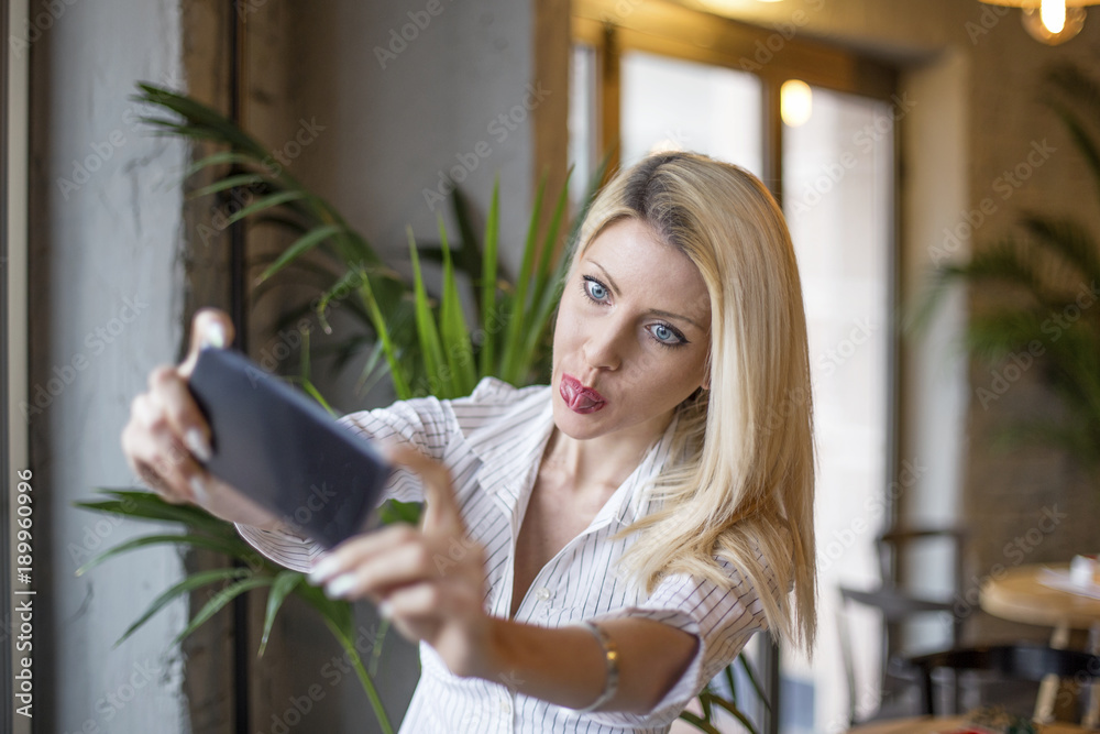 Young blonde girl taking selfie by mobile phone and make a funny face with tongue out Young blonde girl taking selfie by mobile phone and make a funny face with tongue out
