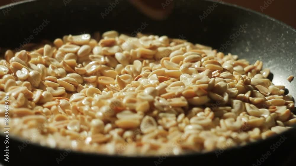 Peeled peanuts are fried in a pan. Hand with a spoon stirring nuts Peeled peanuts are fried in a pan. Hand with a spoon stirring nuts