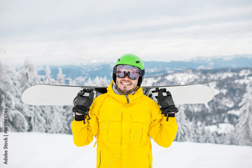 Portrait of a man dressed in winter sports clothes holding a snowboard at the mountains