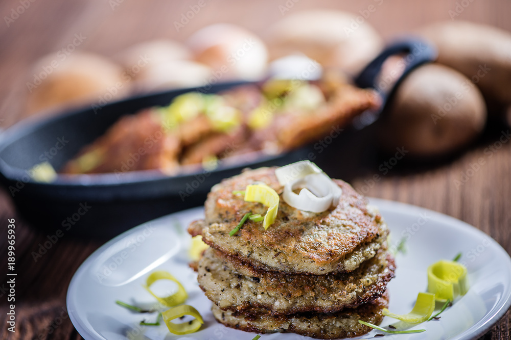 stacked fried potato cakes on white plate with sour cream, spring onion and chives