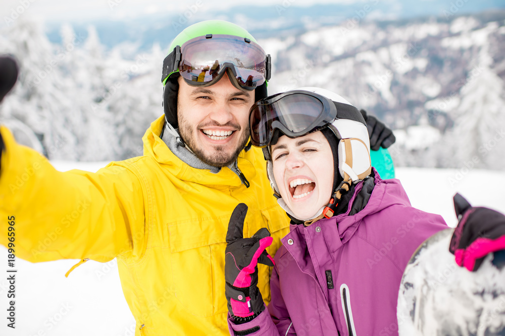 Young couple making selfie portrait standing together in winter sports clothes during the winter vacation on the snowy mountains Young couple making selfie portrait standing together in winter sports clothes during the winter vacation on the snowy mountains