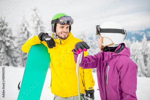 Young couple in winter sports clothes talking together standing with snowboards during the winter vacation on the snowy mountains