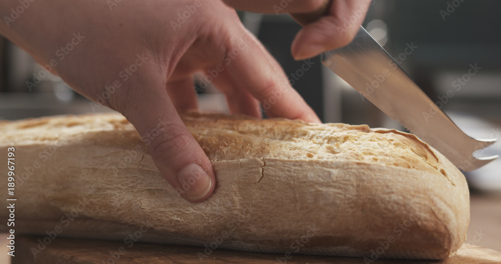 closeup slicing fresh baguette on cutting board