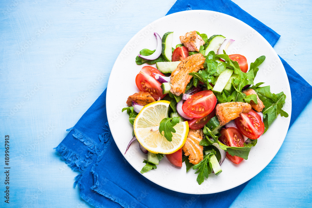 Fresh salad with salmon and vegetables on blue.