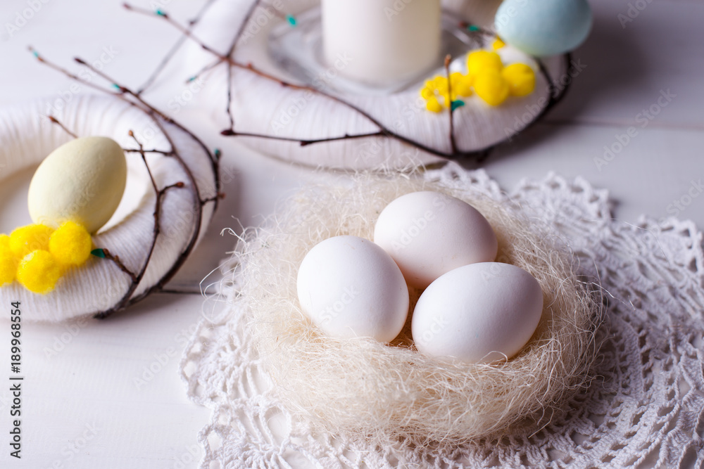 easter decor home - light decor, wreaths, candles and nest with white easter eggs on a white wooden background