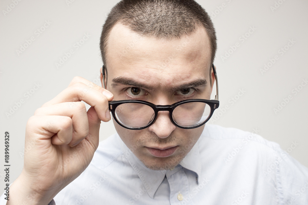 Portrait of young handsome man in blue shirt looking through his glasses. Doctor or businessman or professor style concept. Selective focus and shallow DOF Portrait of young handsome man in blue shirt looking through his glasses. Doctor or businessman or professor style concept. Selective focus and shallow DOF