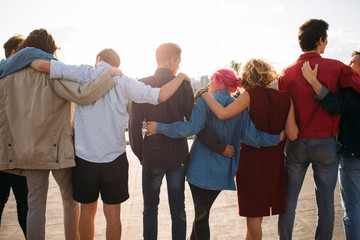 Back view of young diverse people group. Arm around. Unity support. Friendship together