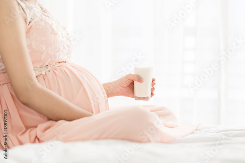 Selective focus Pregnancy woman in pink dress holding a glass of milk on the bed in bedroom.