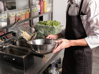 French fries - best junk food ever. Cook preparing fast food in the restaurant kitchen. Unhealthy and unbalanced eating concept