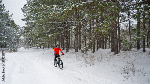 Cyclist in Red Riding Mountain Bike in Beautiful Winter Forest. Extreme Sport and Enduro Biking Concept.