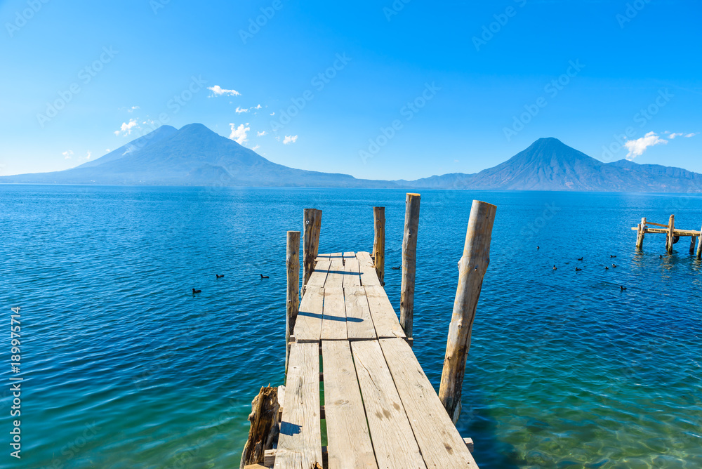 Wooden pier at Lake Atitlan on the beach in Panajachel, Guatemala. With beautiful landscape scenery of volcanoes Toliman, Atitlan and San Pedro in the background. Volcano Highland in Central America.