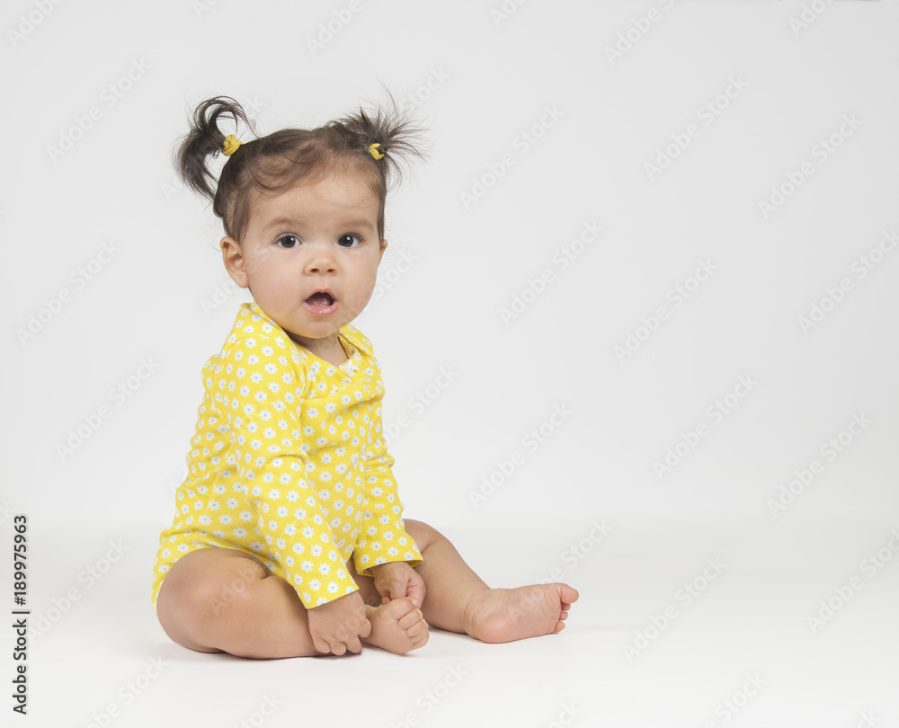 Cute, baby girl in yellow onesie, sitting on white background Photos |  Adobe Stock