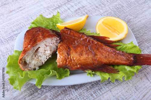 Smoked fish and lemon on green lettuce leaves on Wooden cutting board isolated on white background. photo