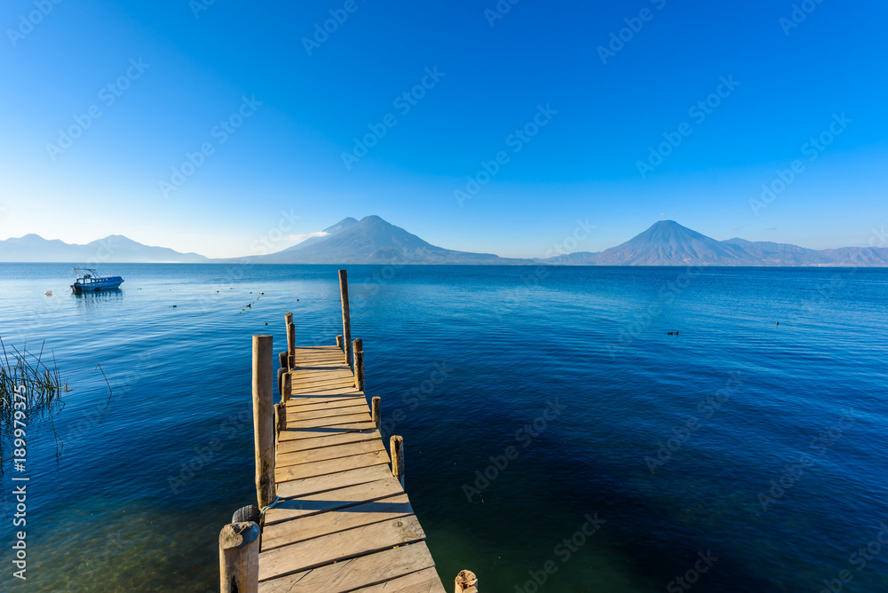 Obraz premium Wooden pier at Lake Atitlan on the beach in Panajachel, Guatemala. With beautiful landscape scenery of volcanoes Toliman, Atitlan and San Pedro in the background. Volcano Highland in Central America.