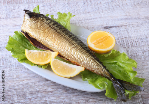 Smoked mackerele and lemon on green lettuce leaves on Wooden cutting board isolated on white background.