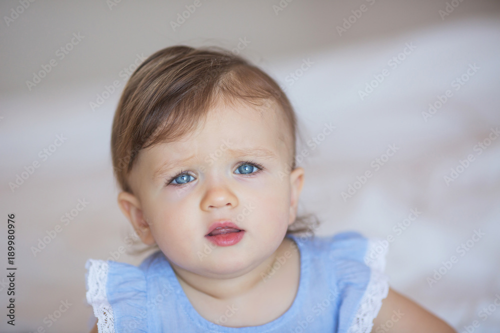 Portrait of pretty little baby girl in a blue dress at home