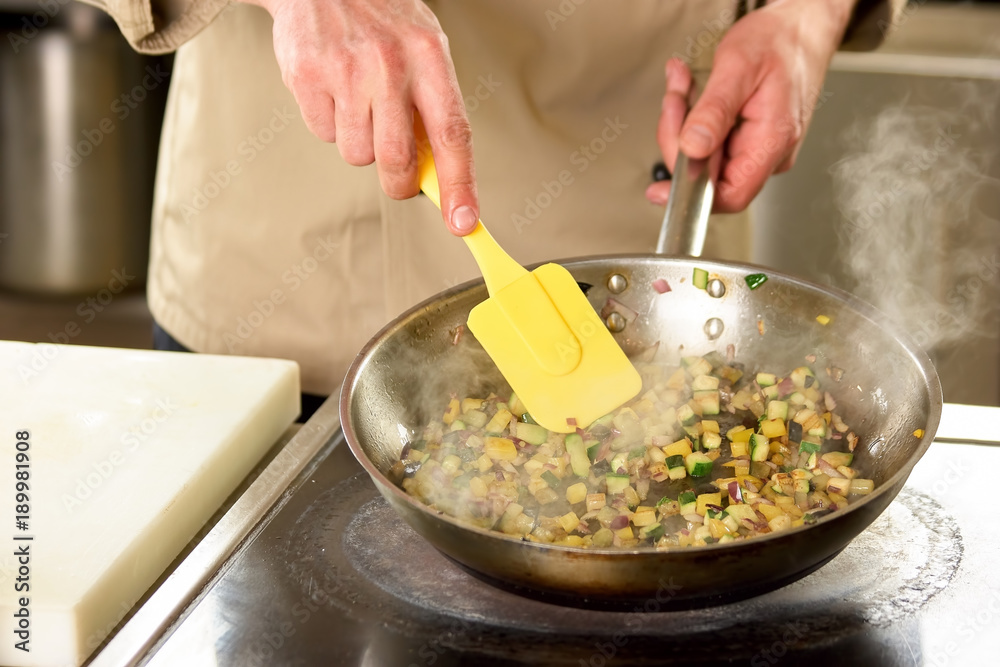 Cooking vegetables in pan using utensil. Cooking diced vegetables in pan using yellow cooking trowel.