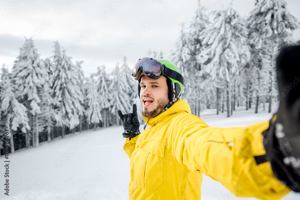 Snowboarder in winter sports clothes making selfie photo outdoors at the snowy mountains