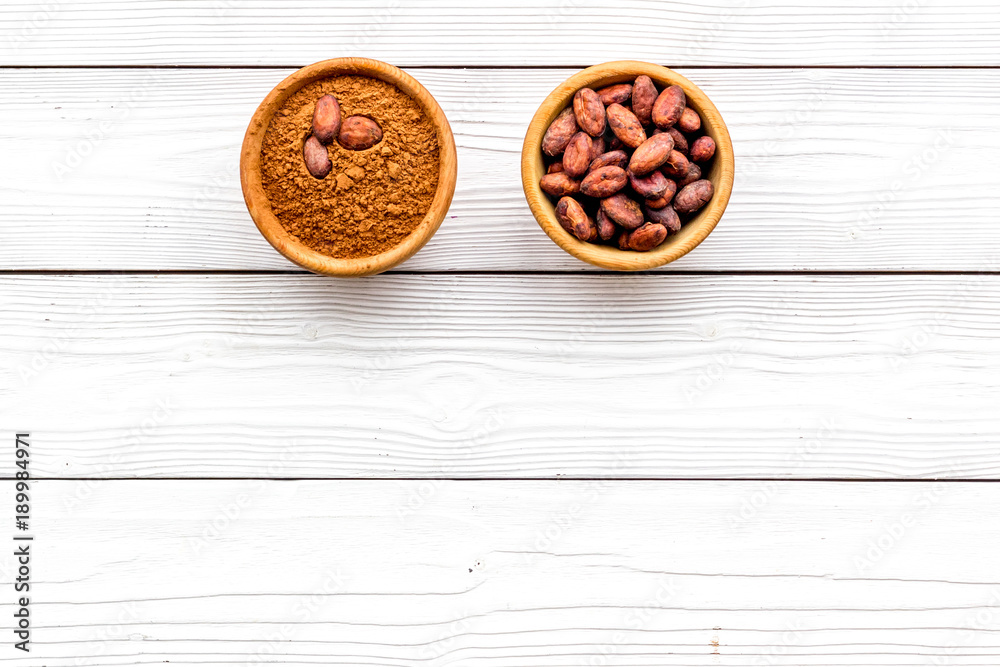 Cocoa powder in bowl and cocoa beans on white wooden background top view copy space. Popular ingregients for sweets, bakery, drinks Cocoa powder in bowl and cocoa beans on white wooden background top view copy space. Popular ingregients for sweets, bakery, drinks